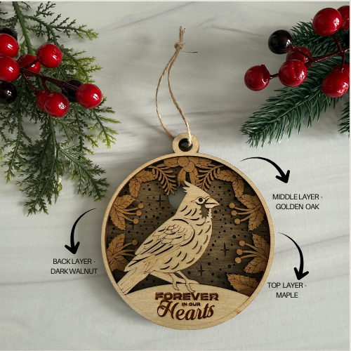 Wooden ornament with bird design and 'Forever in Our Hearts' text, surrounded by Christmas decorations.