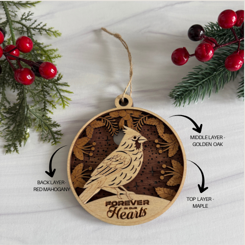 Wooden ornament with bird design and 'Forever in Our Hearts' text, surrounded by Christmas decorations.
