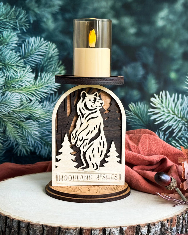A rustic wooden bear-shaped candle holder with a lit LED candle on top, displayed on a tree stump slice with pine branches and autumn leaves in the background.