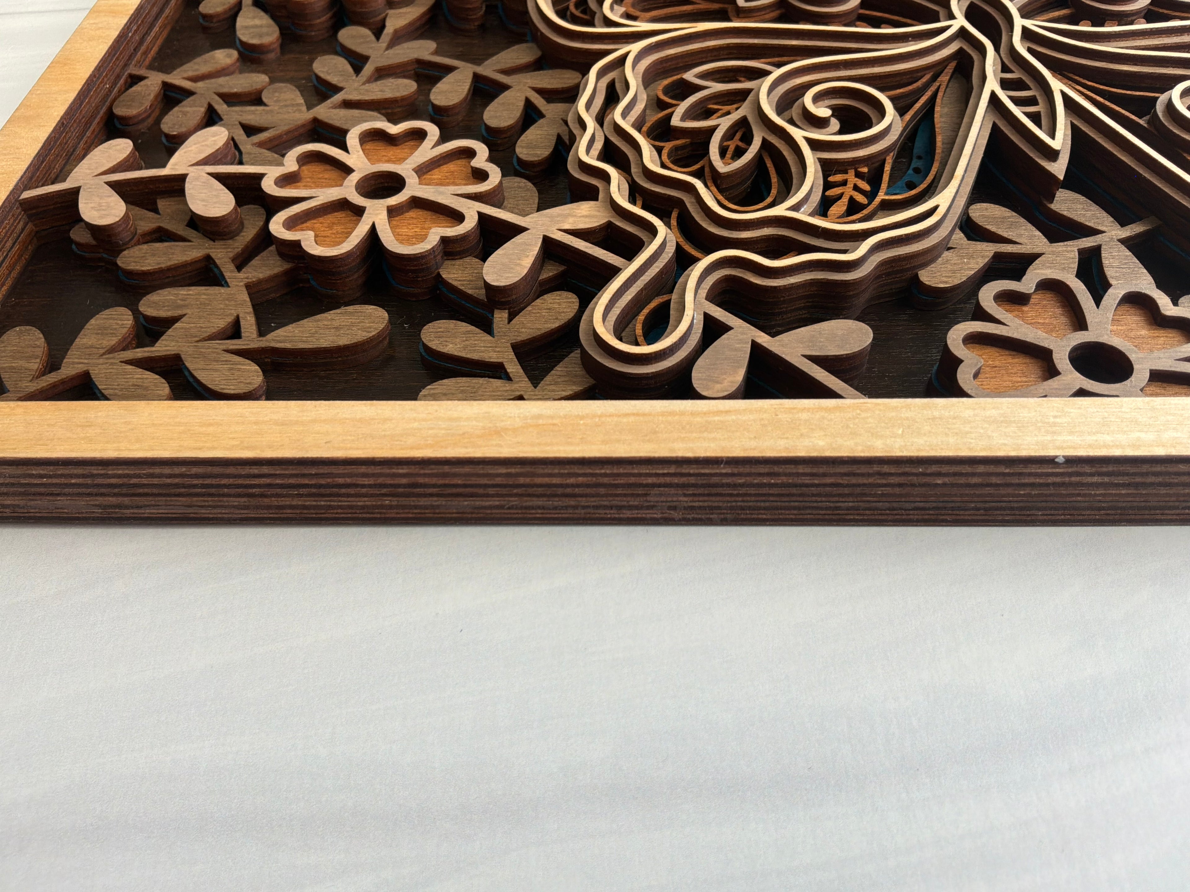 Close-up angled view of 5-layer butterfly wood art showing the physical depth, floral cutouts, and natural shadows of the multidimensional design.