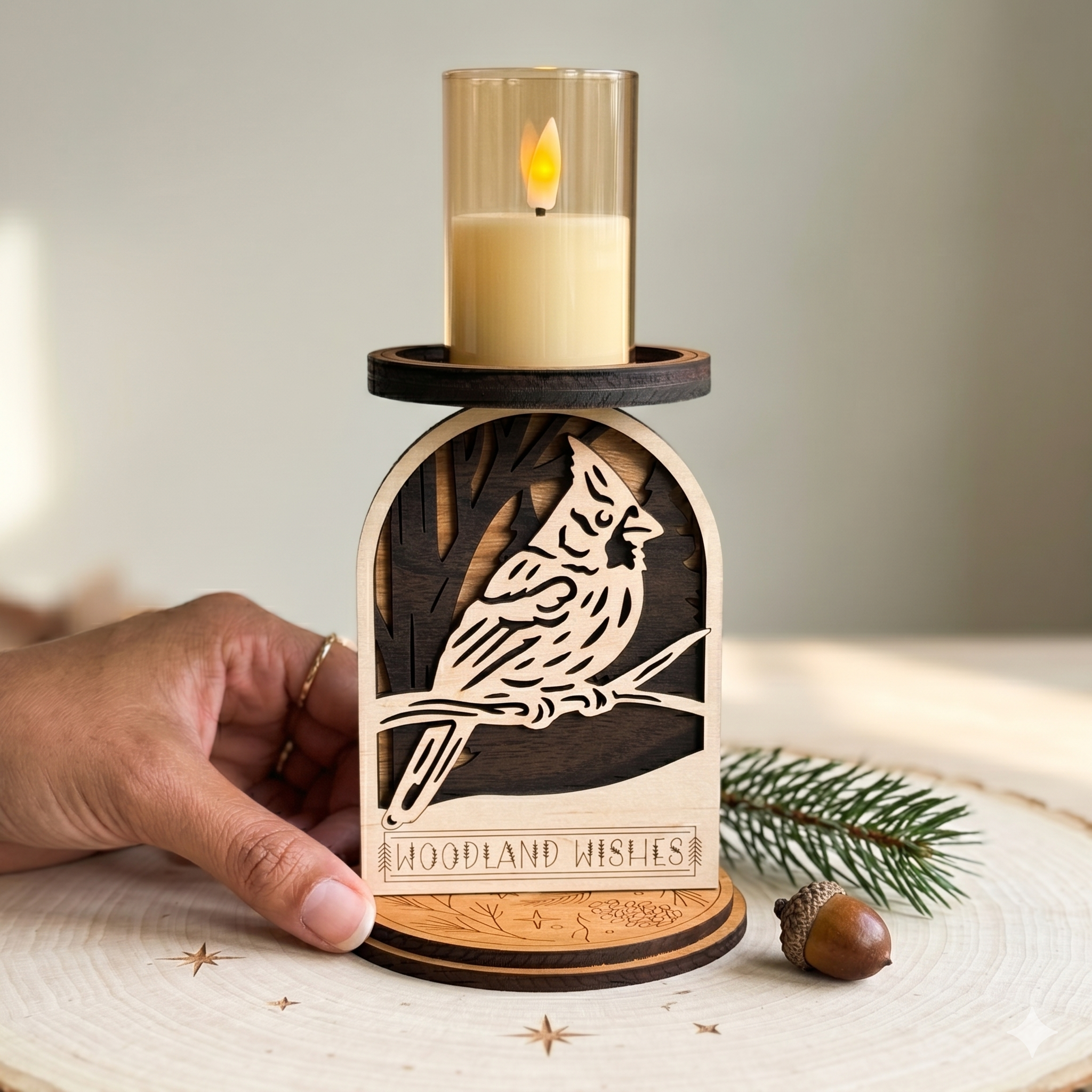 Wooden candle holder with cardinal design and 'Woodland Wishes' text, held by a hand on a neutral background by Cactus Air Designs.
