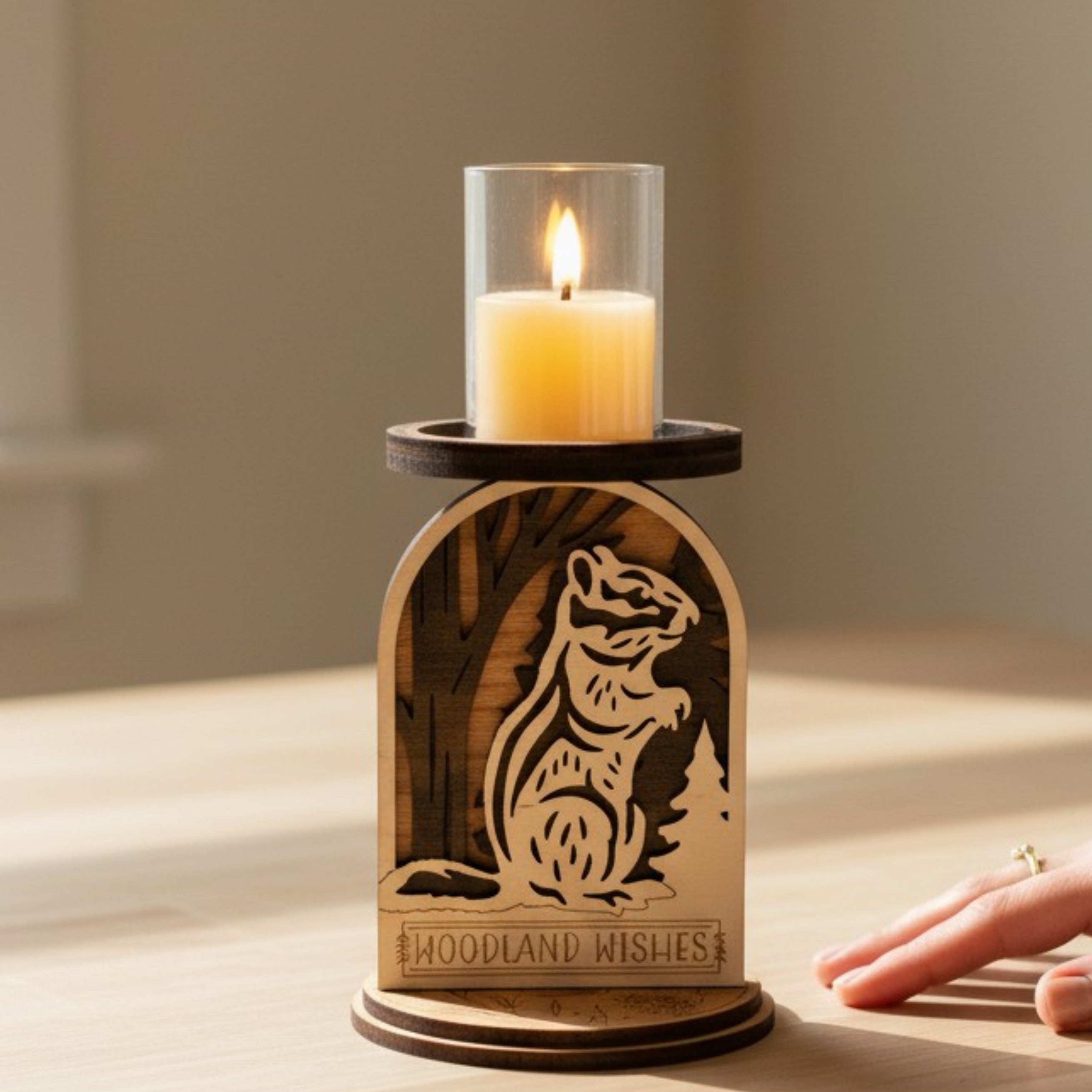 Wooden candle holder with a squirrel design and 'Woodland Wishes' text, featuring a lit candle with hand by it to show size by Cactus Air Designs. 
