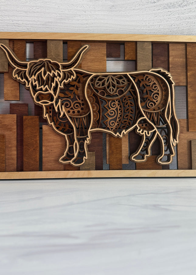 Front view of a 3D layered Highland Cow wall art featuring five intricate laser-cut wood layers and warm golden oak to red mahogany stained bar background