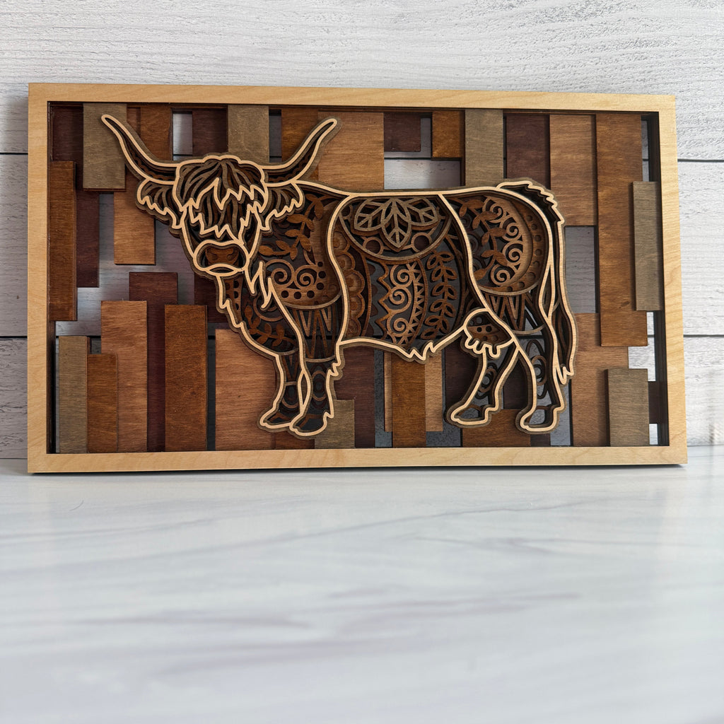 Front view of a 3D layered Highland Cow wall art featuring five intricate laser-cut wood layers and warm golden oak to red mahogany stained bar background