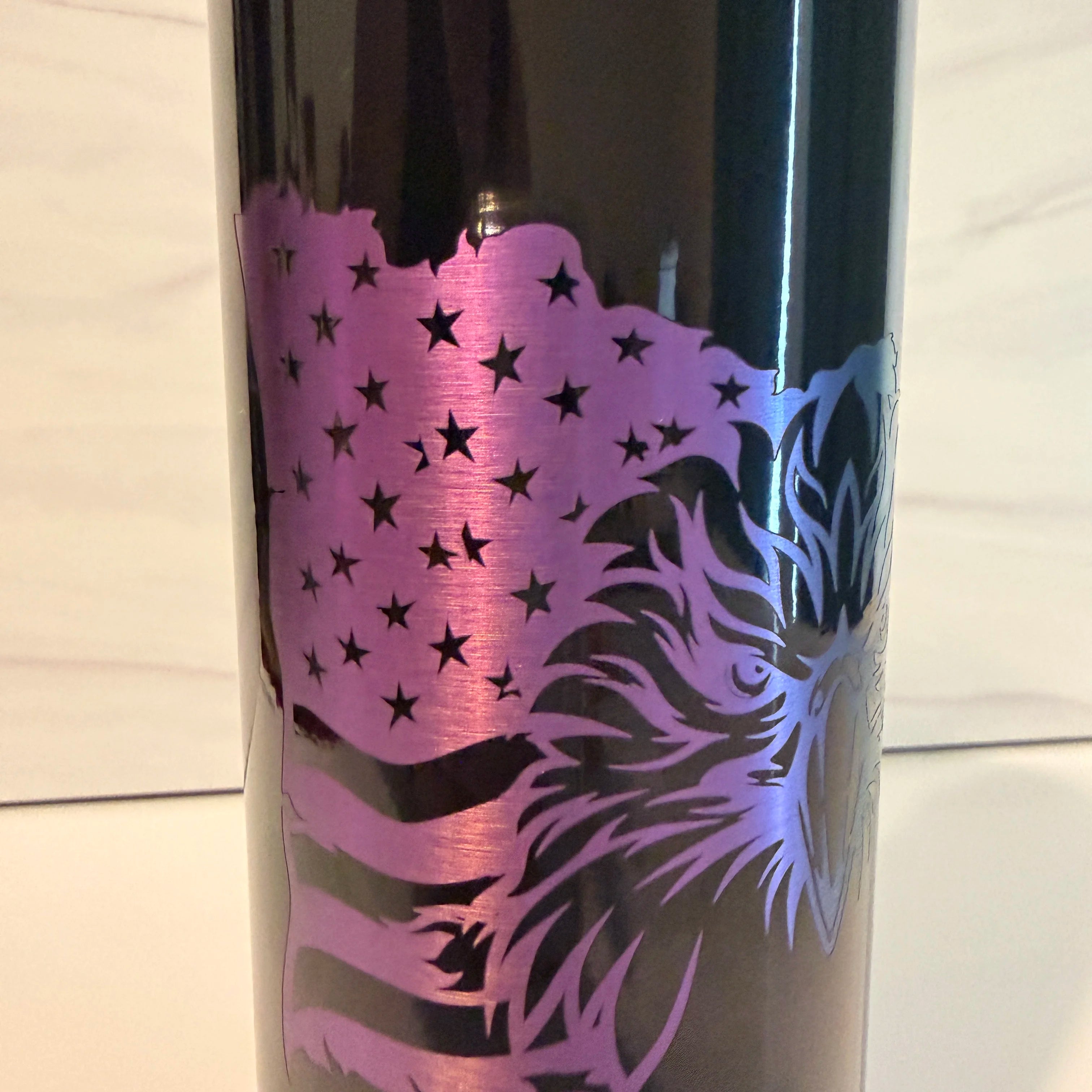 Detailed closeup of patriotic eagle laser engraving on black tumbler showing purple and blue electroplate layer with stars and feathers detail
