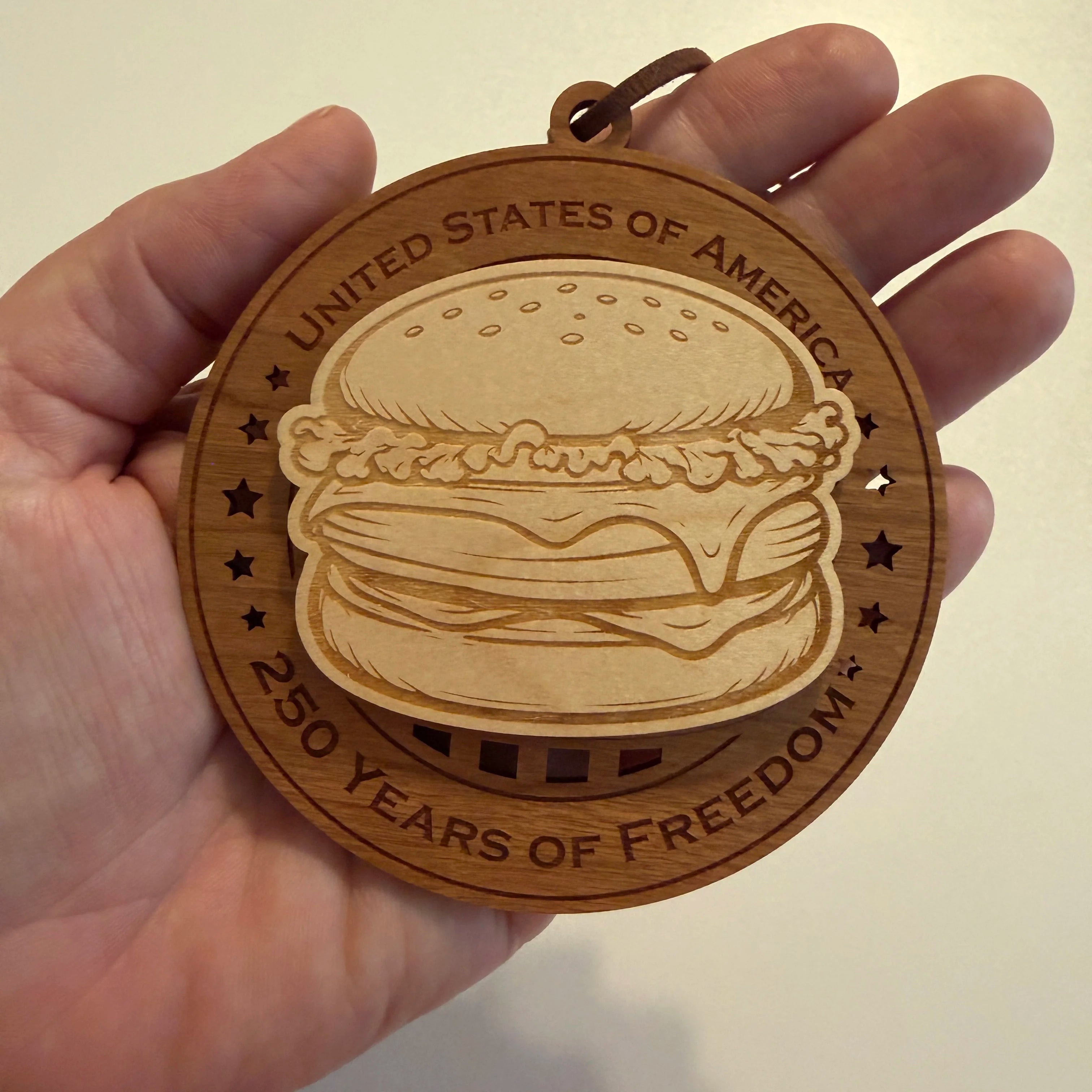 Hand holding USA 250th Anniversary Cheeseburger wood ornament showing actual size approximately 3.5 inches handcrafted by Cactus Air Designs Arizona