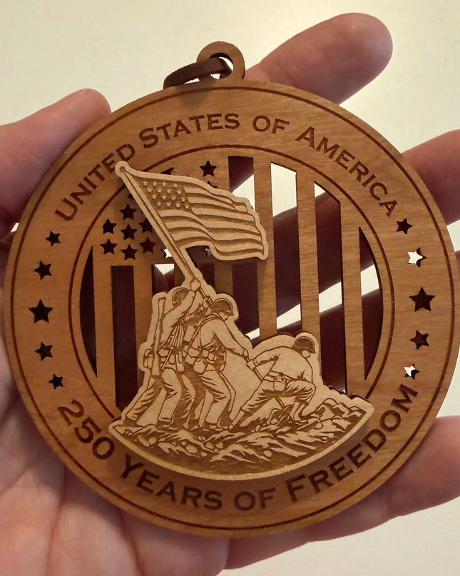 Hand holding USA 250th Anniversary Flag Raising wood ornament showing actual size approximately 3.5 inches handcrafted by Cactus Air Designs Arizona