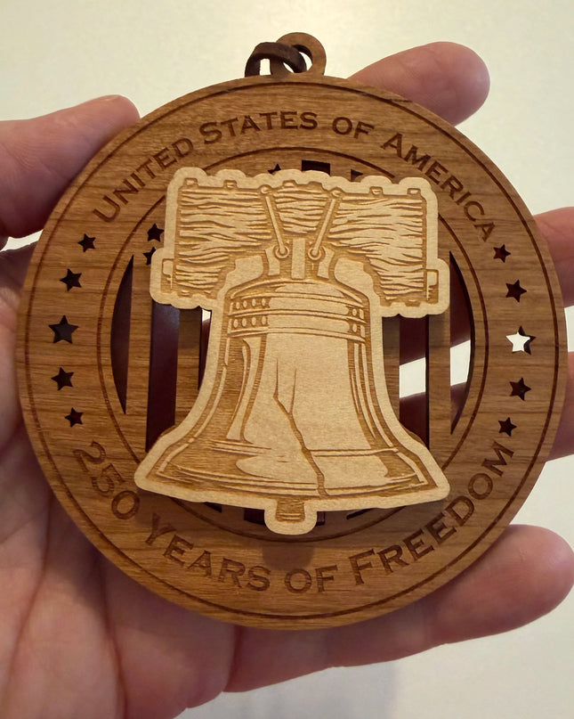 Hand holding USA 250th Anniversary Liberty Bell wood ornament showing actual size approximately 3.5 inches handcrafted by Cactus Air Designs Arizona