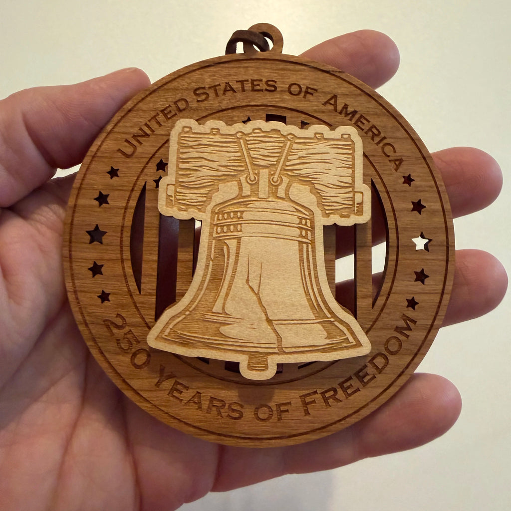 Hand holding USA 250th Anniversary Liberty Bell wood ornament showing actual size approximately 3.5 inches handcrafted by Cactus Air Designs Arizona