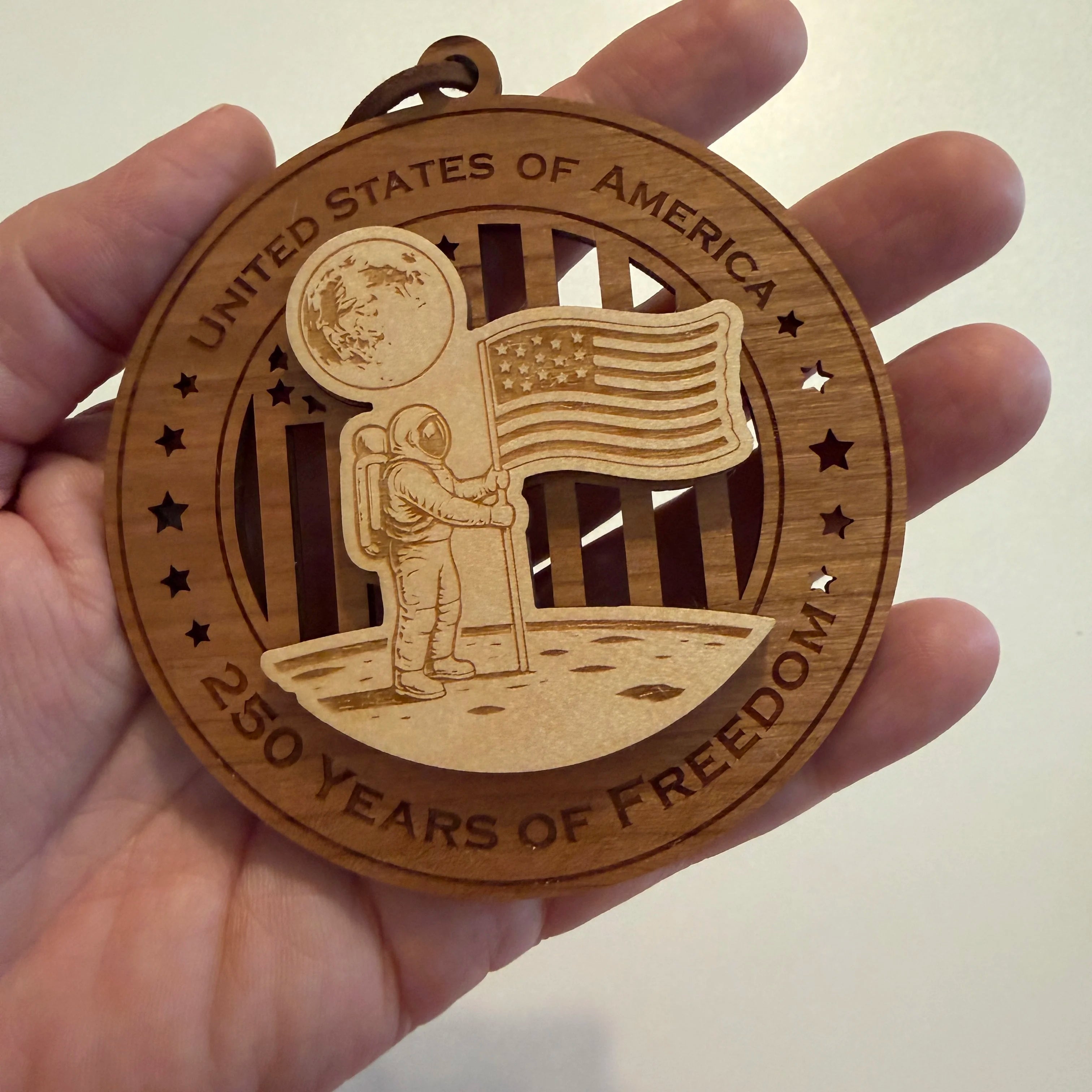 Hand holding USA 250th Anniversary Moon Landing wood ornament showing actual size approximately 3.5 inches handcrafted by Cactus Air Designs Arizona