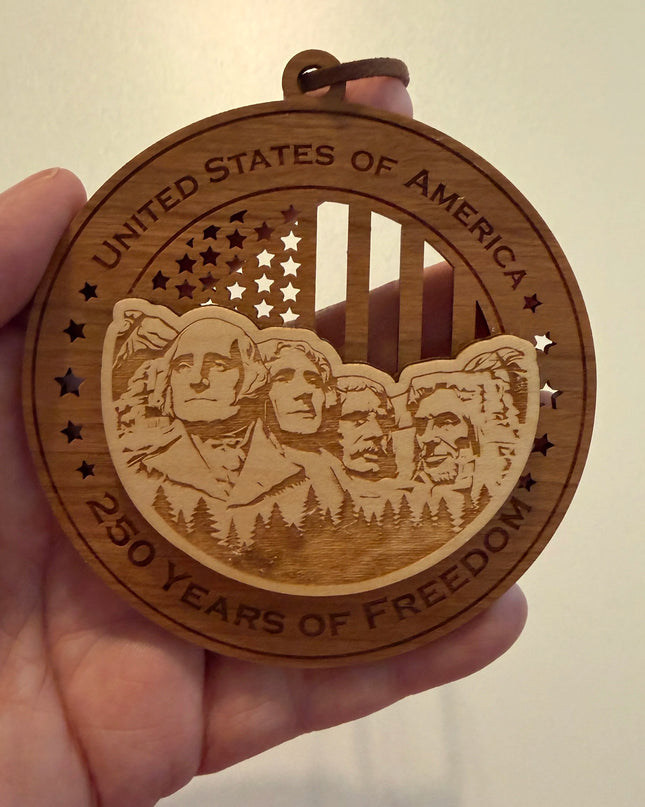 Hand holding USA 250th Anniversary Mount Rushmore wood ornament showing actual size approximately 3.5 inches handcrafted by Cactus Air Designs Arizona