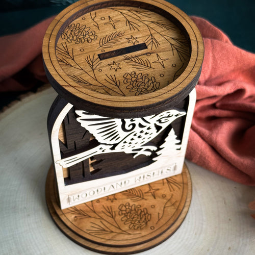 Wooden lantern with laser-cut design of a bird and floral patterns on a white surface.