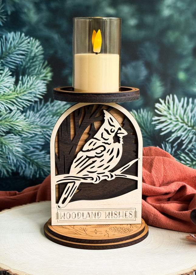 Wooden candle holder with cardinal design and lit candle against a green foliage background