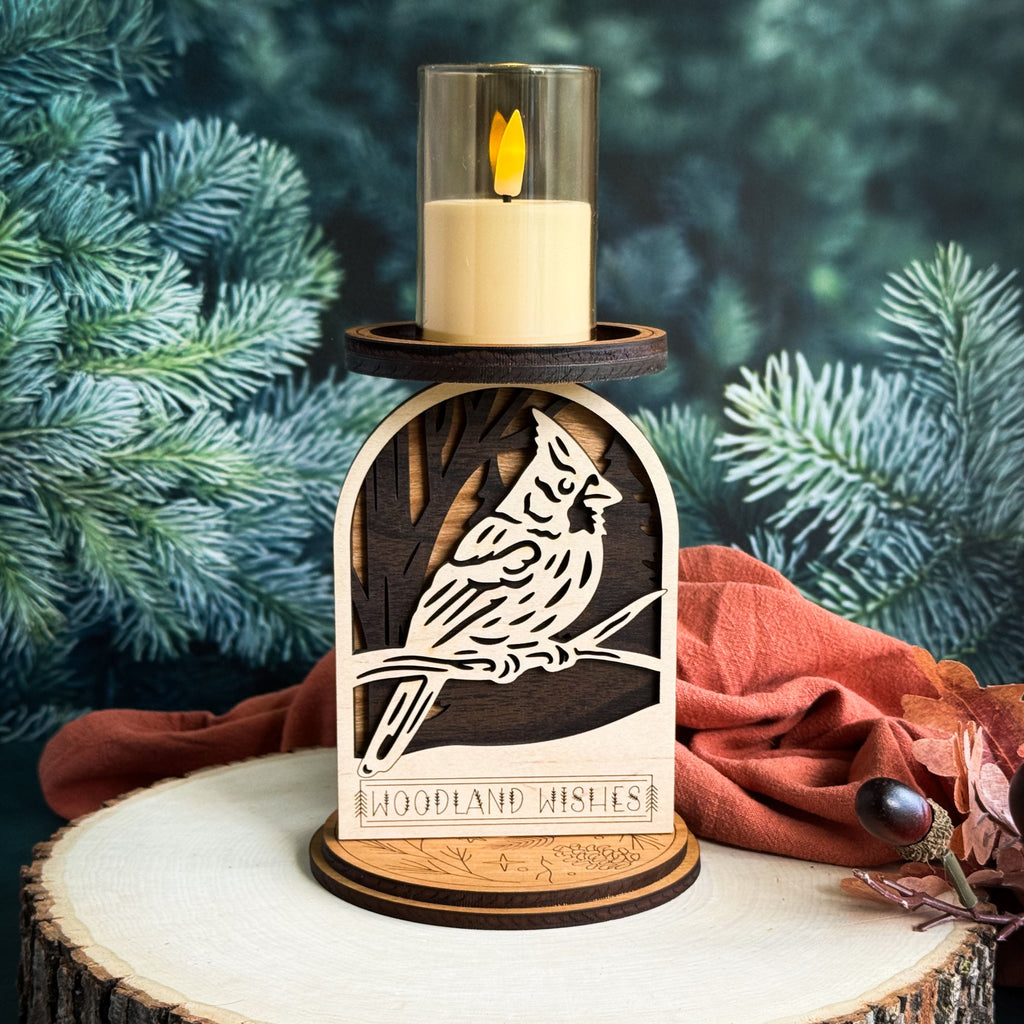 Wooden candle holder with cardinal design and lit candle against a green foliage background