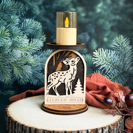 Decorative candle holder with fawn design on a wooden base against a green foliage background