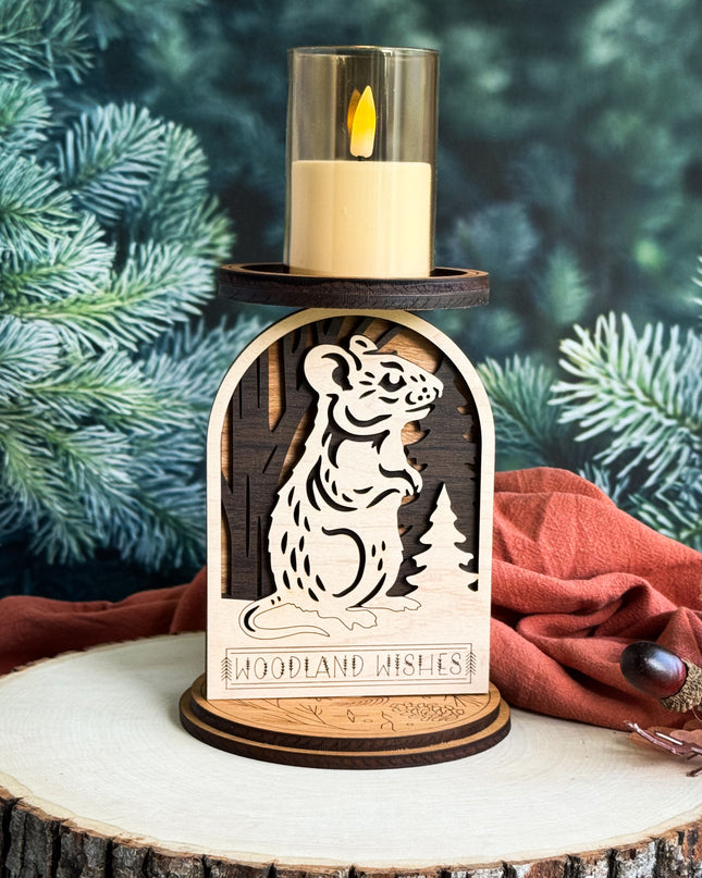 Wooden candle holder with tiger design and 'Woodland Wishes' text, lit candle inside, against a green foliage background.