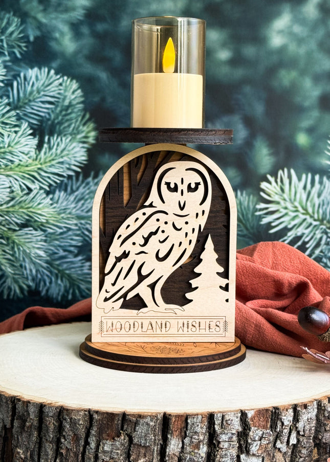 Decorative candle holder with owl design on a wooden base, surrounded by pine branches and leaves.