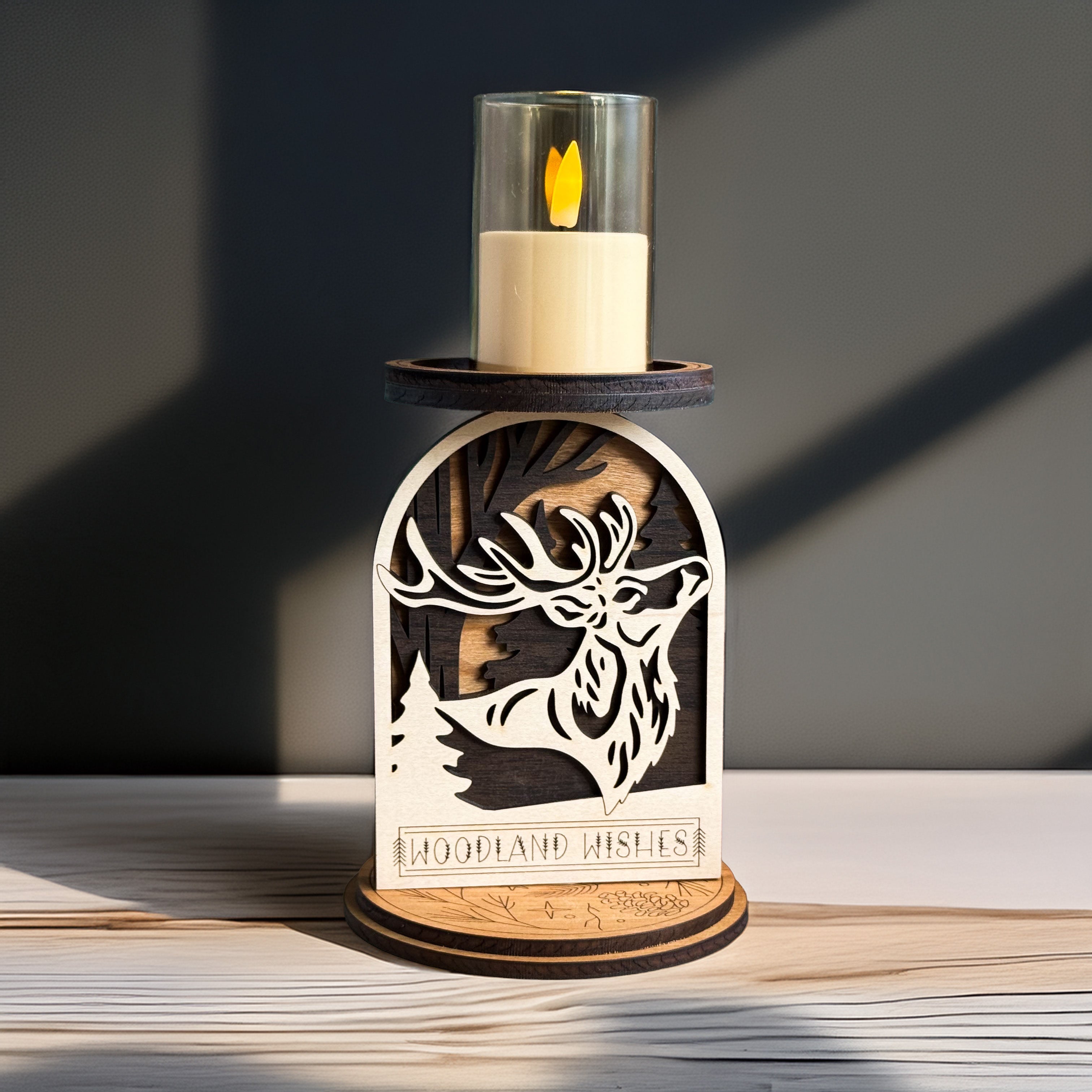 Decorative candle holder with a cut-out design of a deer and the text 'Woodland Wishes' on a wooden surface.