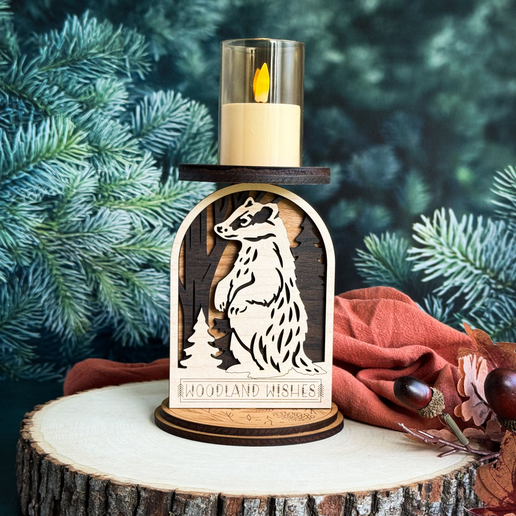 Wooden candle holder with weasel design and 'Woodland Wishes' text, against a green foliage background.