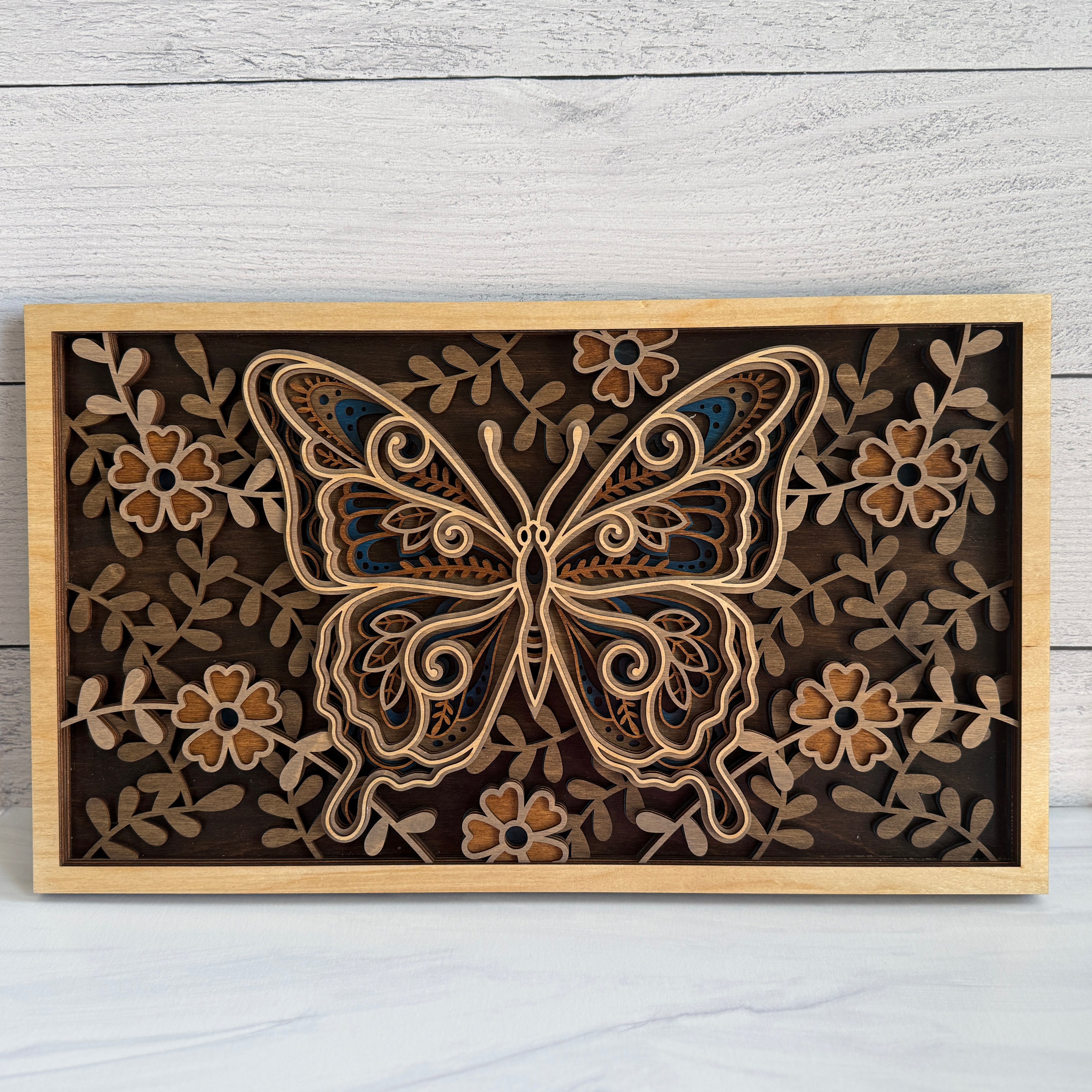Front view of a 3D layered butterfly wood wall art featuring five intricate laser-cut layers with floral patterns in natural and blue wood stains.