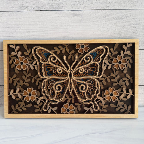 Front view of a 3D layered butterfly wood wall art featuring five intricate laser-cut layers with floral patterns in natural and blue wood stains.