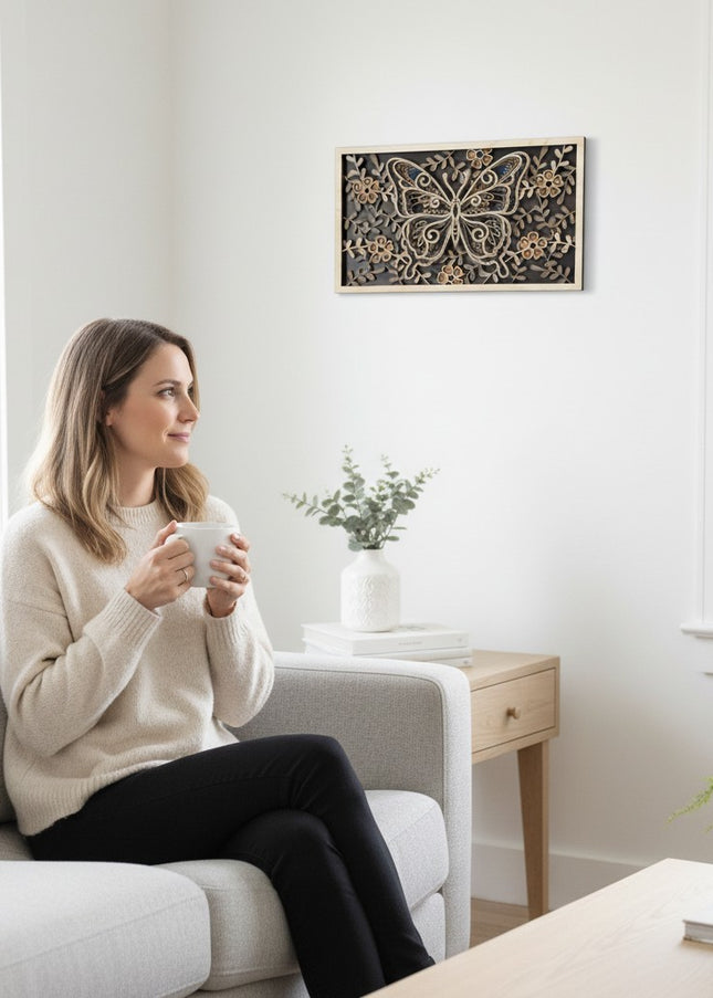 Person holding a coffee mug admiring a 3D layered butterfly wood wall art on a white wall showing the scale of the 18 by 10.5 inch piece