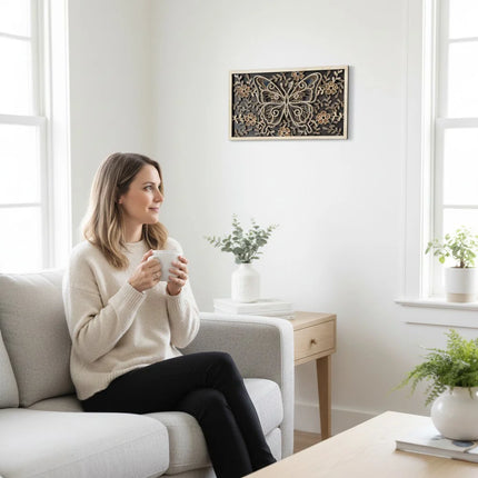 Woman sitting on a couch holding a mug in a bright living room with plants and a layered butterfly wood wall art on the wall. 