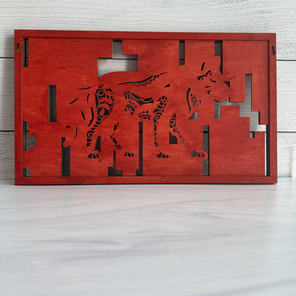 A rectangular red wooden back of wall art piece featuring a stylized wolf silhouette with cutout geometric patterns, displayed against a white wood-paneled wall on a light surface.