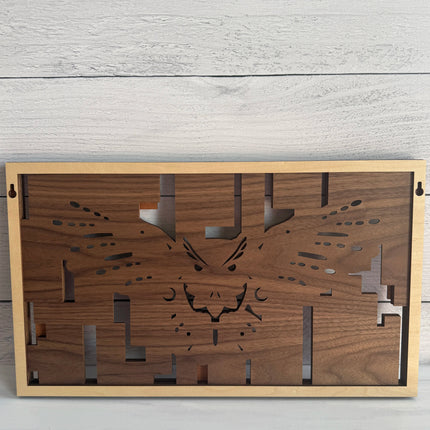A rectangular wooden wall art piece with a laser-cut animal face design, featuring a natural walnut wood center and a light natural wood frame, displayed against a light gray wood plank background.