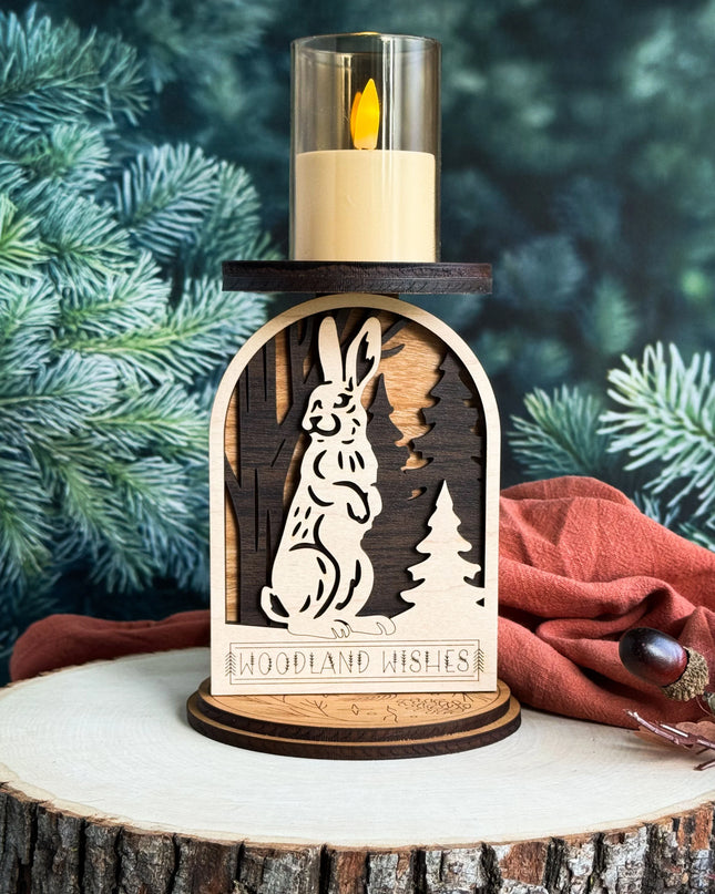 Layered wood woodland rabbit candle holder with LED candle lit, displayed on a wood slice with pine branches in background