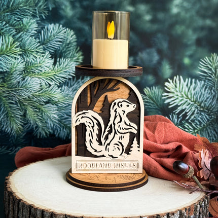 Layered wood woodland skunk candle holder with LED candle lit, displayed on a wood slice with pine branches in background