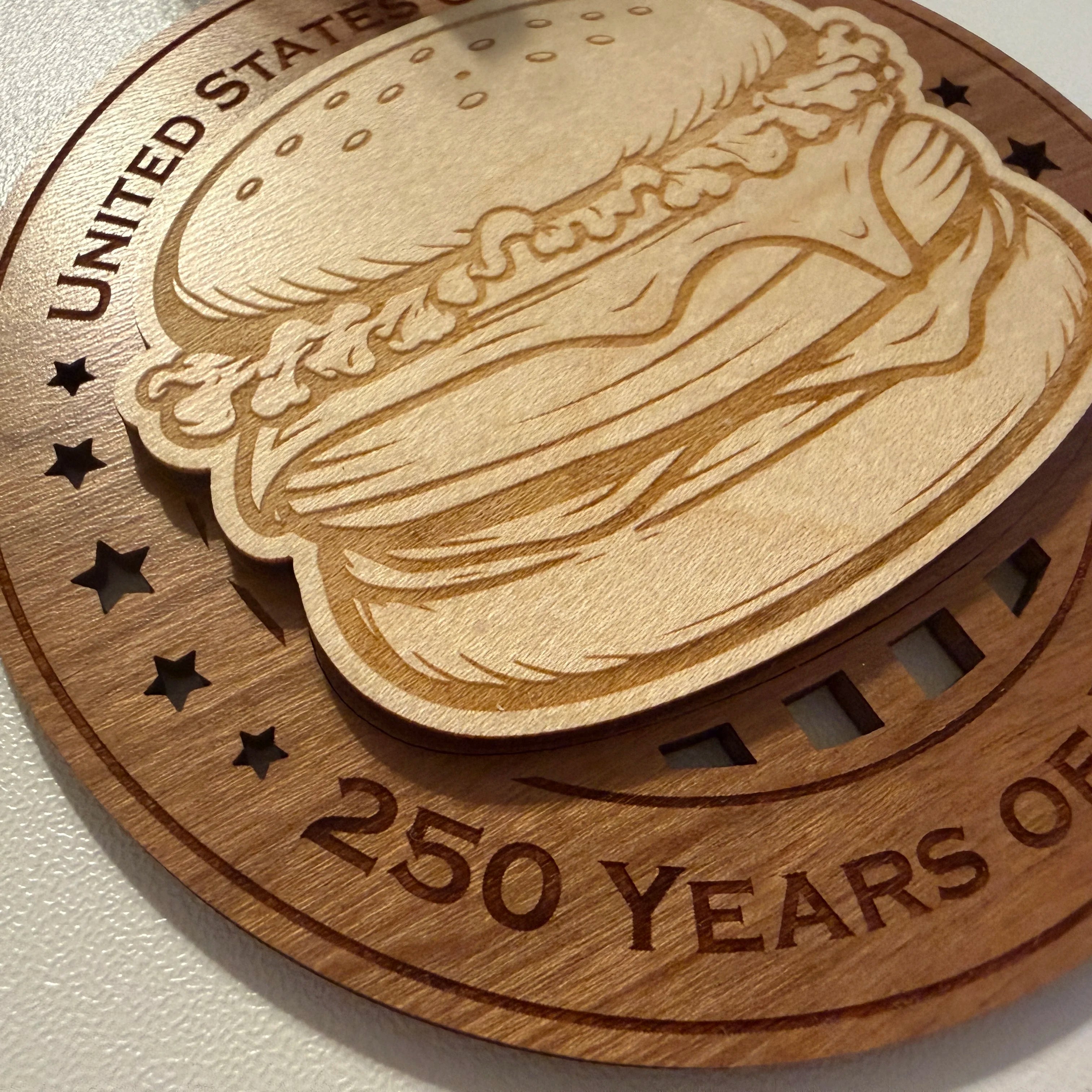 Close up detail of laser engraving on USA 250th Anniversary Cheeseburger wood ornament showing Premium Cherry plywood and Maple plywood layers