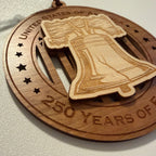 Close up detail of laser engraving on USA 250th Anniversary Liberty Bell wood ornament showing Premium Cherry plywood and Maple plywood layers