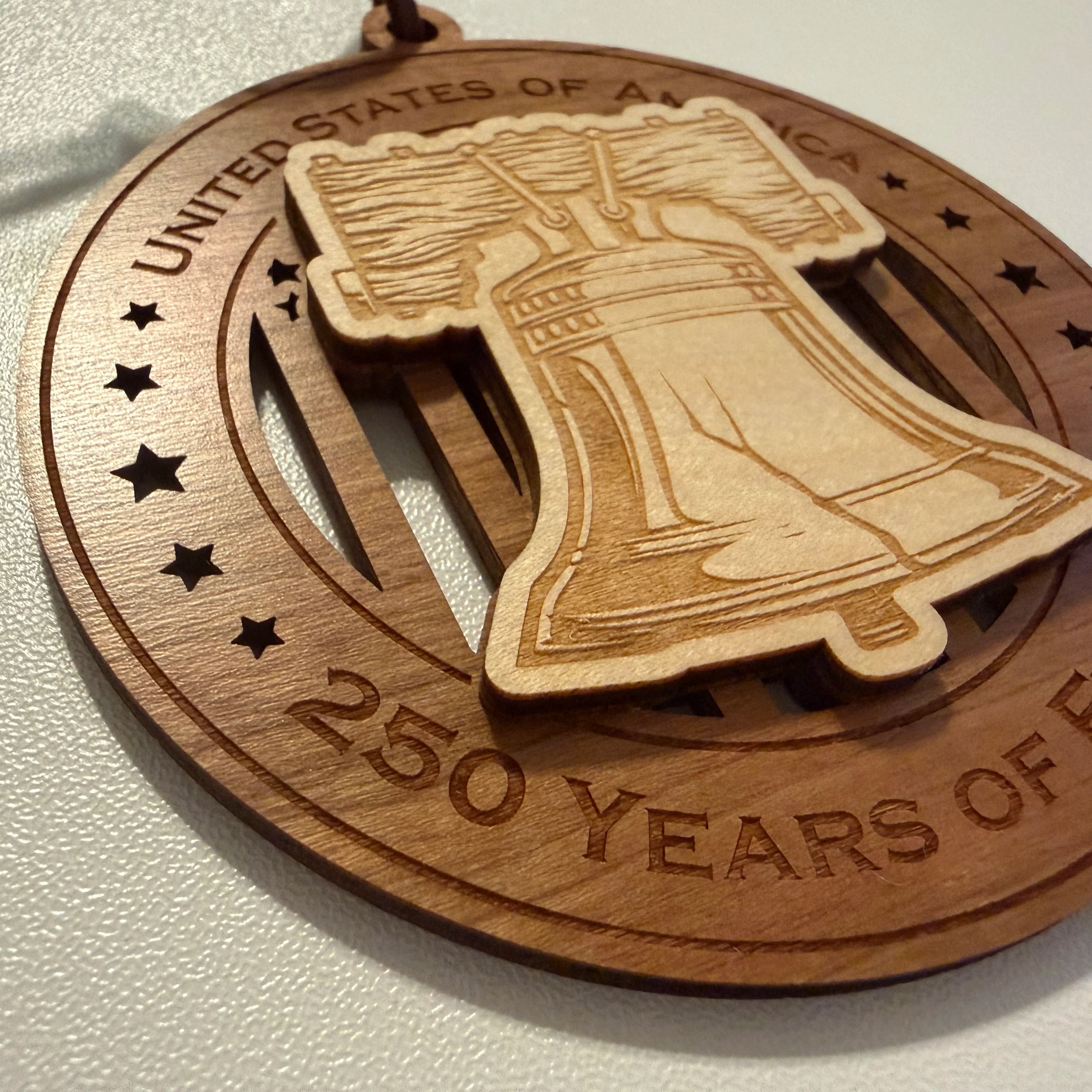 Close up detail of laser engraving on USA 250th Anniversary Liberty Bell wood ornament showing Premium Cherry plywood and Maple plywood layers