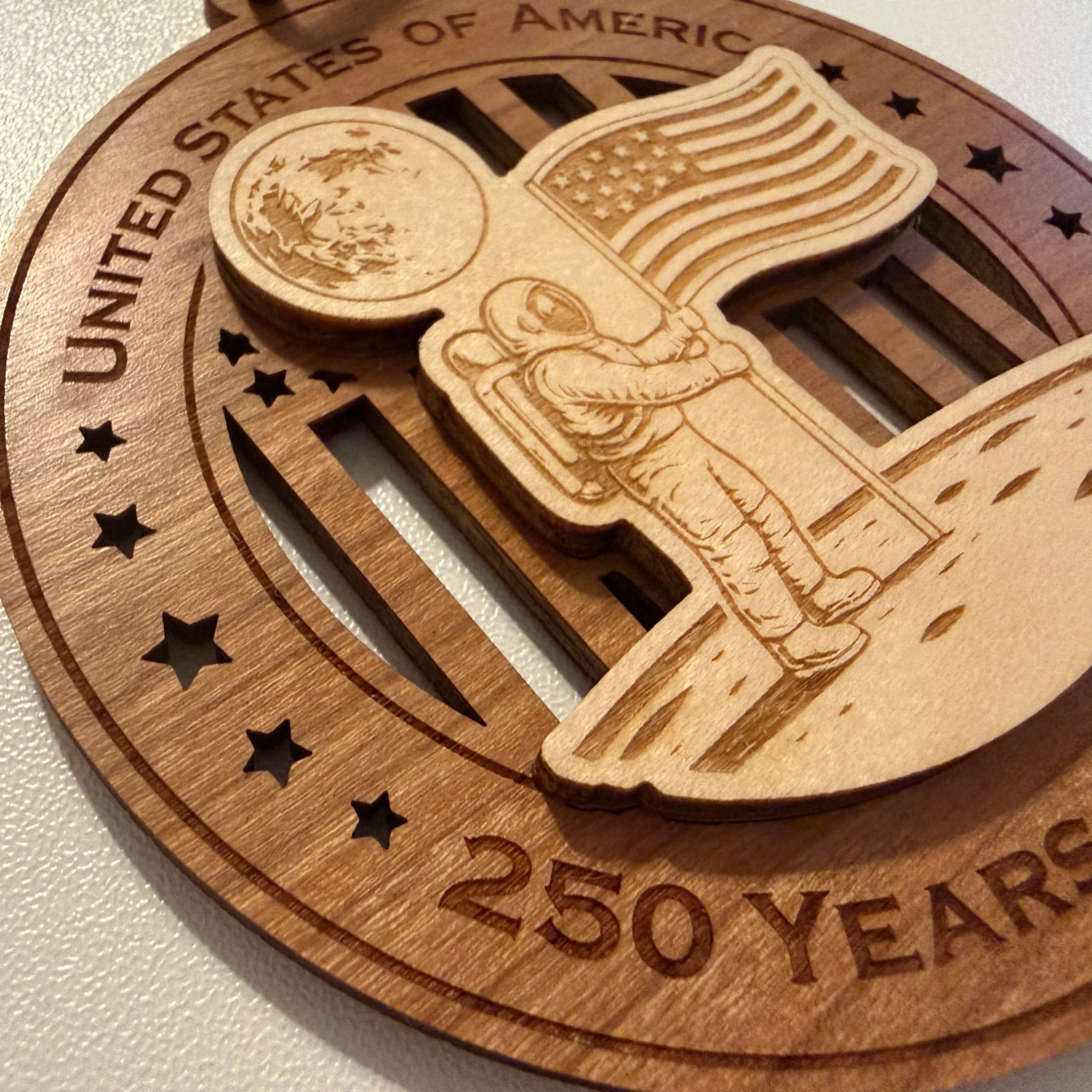 Close up detail of laser engraving on USA 250th Anniversary Moon Landing wood ornament showing Premium Cherry plywood and Maple plywood layers