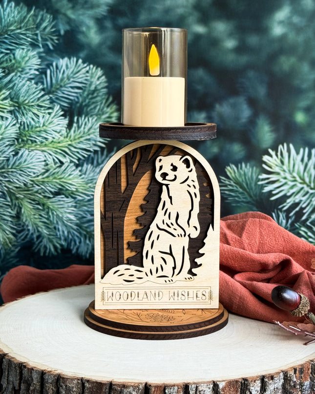 Layered wood woodland weasel candle holder with LED candle lit, displayed on a wood slice with pine branches in background
