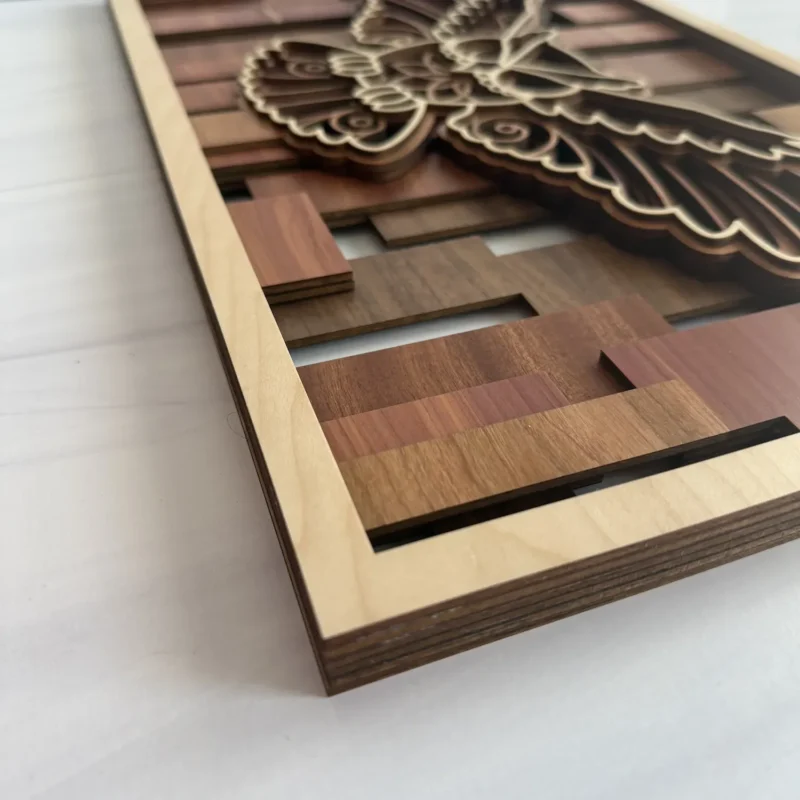 Corner angle of owl layered wall art showing stacked wood species layers and mosaic slat background with natural maple frame edge