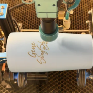 Laser rotary tool engraving a custom design onto a powder-coated tumbler in the studio