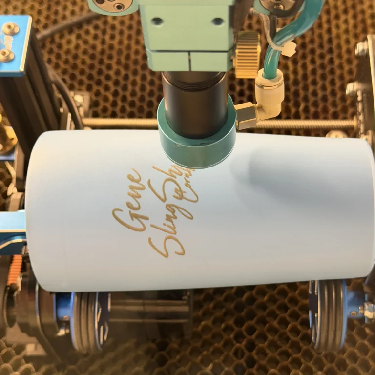 Laser rotary tool engraving a custom design onto a powder-coated tumbler in the studio