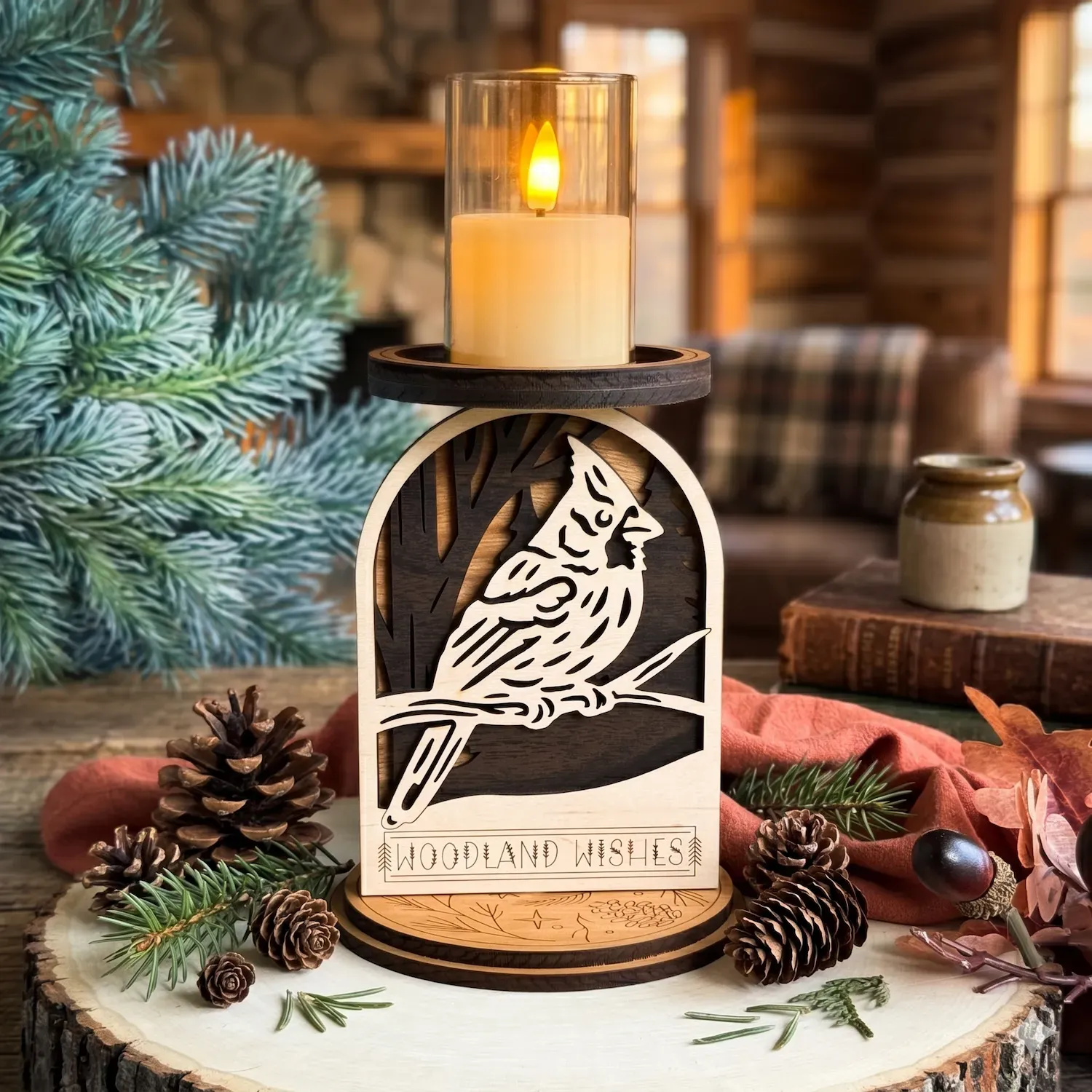 Layered wood cardinal candle holder with Woodland Wishes engraving on a wood slice with pine branches and pinecones, stone fireplace glowing with warm golden light and stacked antique books in background