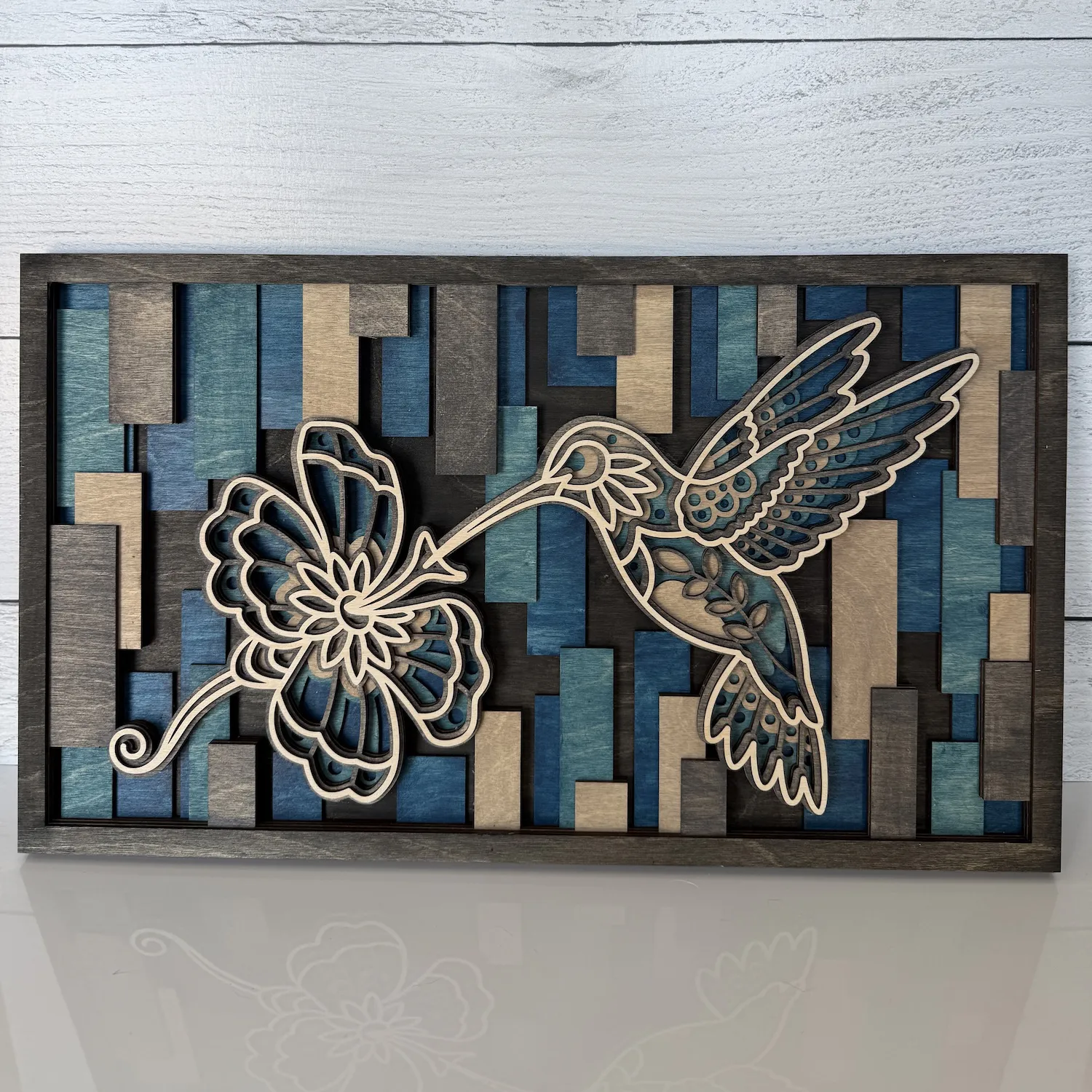 Front view of six-layer maple wood art featuring a hummingbird, flower, and geometric background in cool desert colors.
