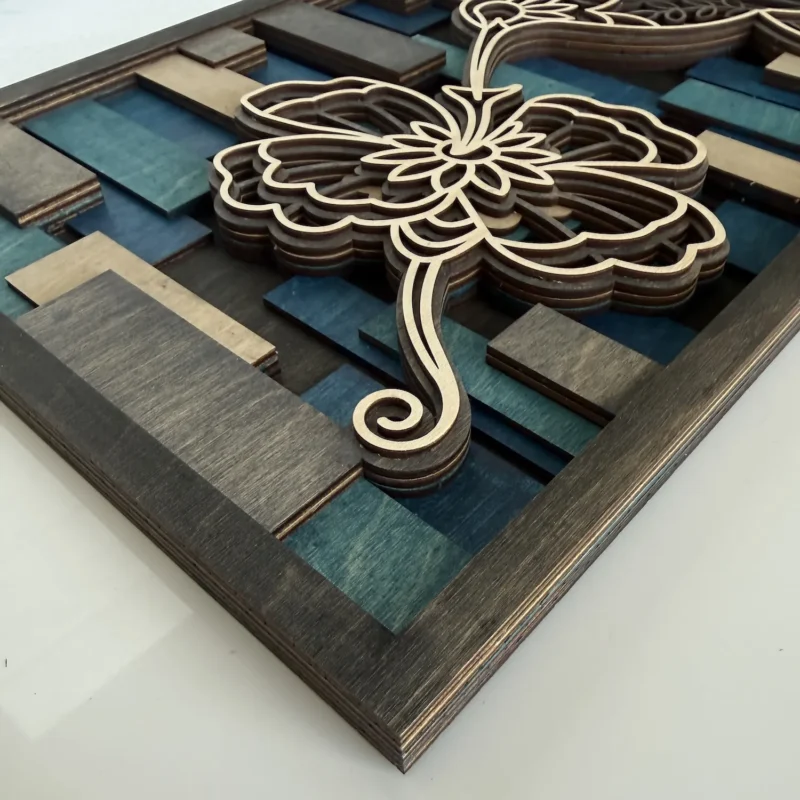 Handcrafted layered wood hummingbird hovering beside a flower in teal, navy, grey, and natural maple stains.