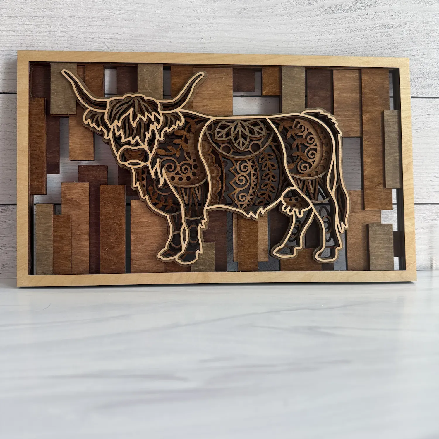 Layered highland cow wall art with mandala engravings, natural maple frame, and mosaic stained slat background