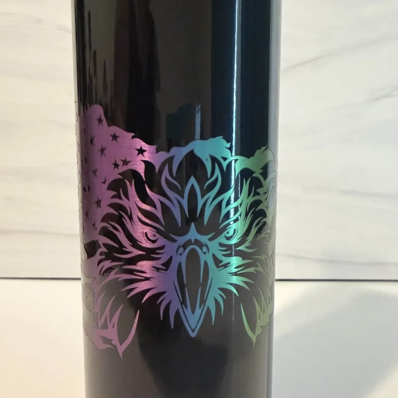 Laser-engraved bald eagle face detail on black electroplated 20 oz skinny tumbler with iridescent rainbow color shift from purple to teal to green