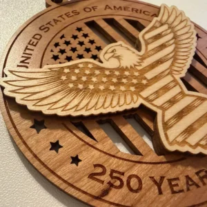 Close-up detail of a layered wooden ornament showing a raised bald eagle with outstretched wings, laser-engraved stars across its body and stripes across its wings and tail, over a cut-through American flag background.
