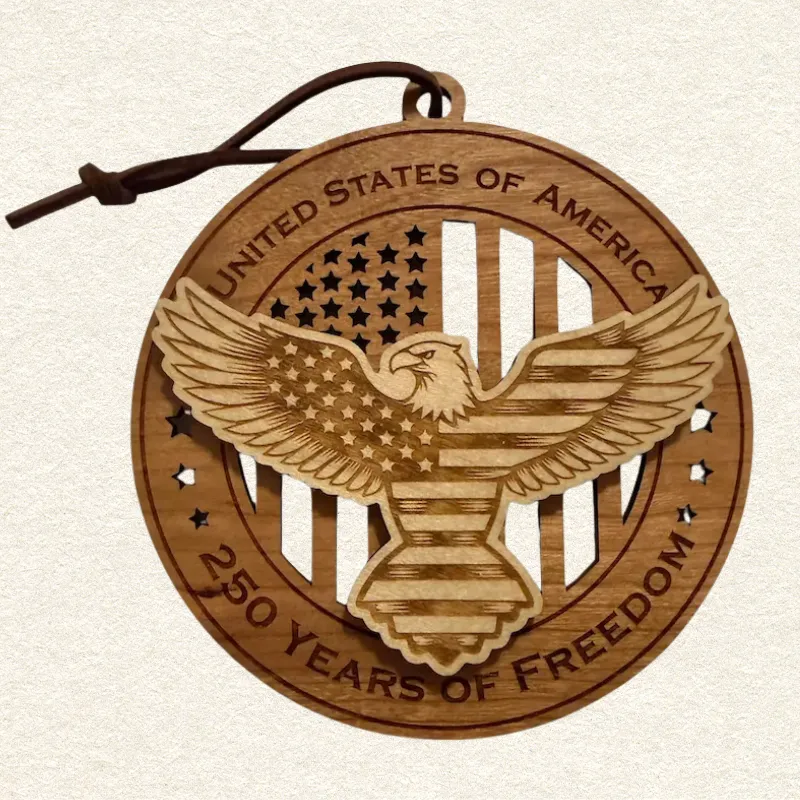 Round two-tone wood ornament featuring a spread-wing bald eagle patterned with stars and stripes, engraved “United States of America” and “250 Years of Freedom.”