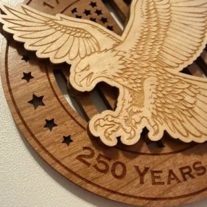 Close-up detail of a layered wooden ornament showing a raised bald eagle swooping forward with spread wings, extended talons, and finely laser-engraved feather details over a cut-through American flag background.
