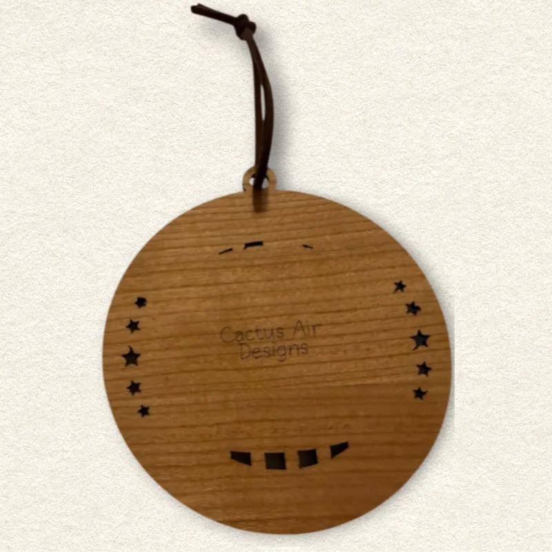 Back of the round wooden ornament showing the natural wood grain, an attached brown hanging cord, and “Cactus Air Designs” laser engraved in a delicate single-line font.