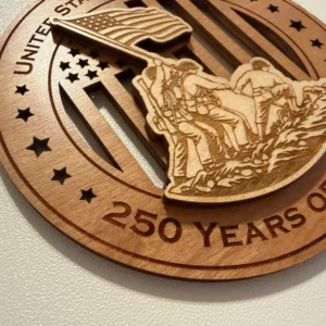 Close-up detail of a layered wooden ornament depicting service members raising the American flag at Iwo Jima, with finely laser-engraved uniforms, equipment, flag details, and rocky terrain over a cut-through flag background.