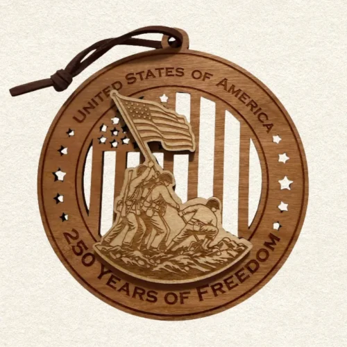 Round two-tone wood ornament depicting the Iwo Jima flag raising over stars and stripes, engraved “United States of America” and “250 Years of Freedom" and hung on a brown cord